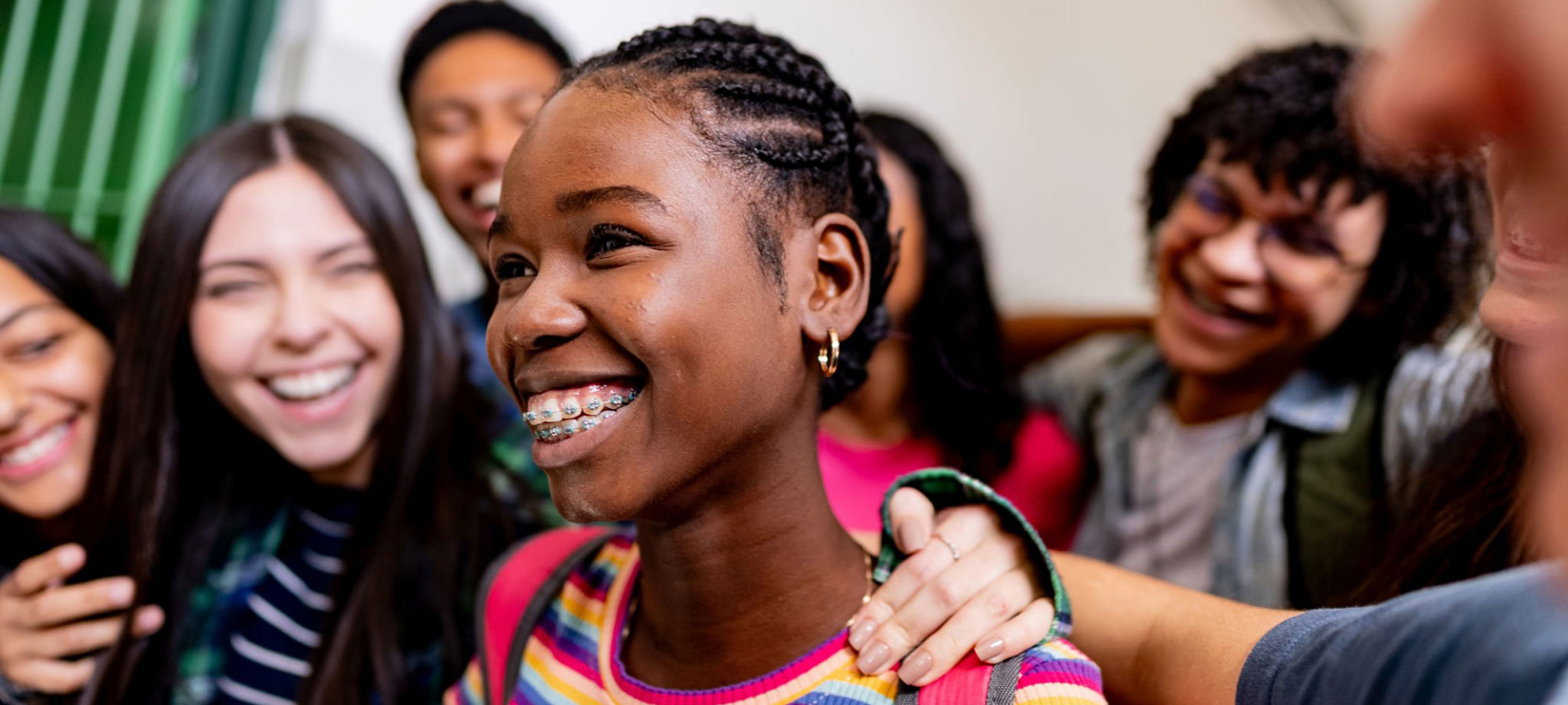 A young student wears a back pack and smiles while surrounded by classmates.